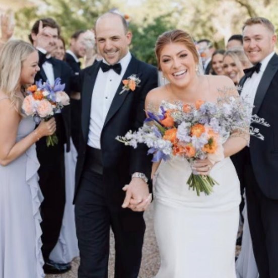 A newly married bride and groom smiling as their bridal party looks on. This couple represents the joy of weddings in Fredericksburg TX