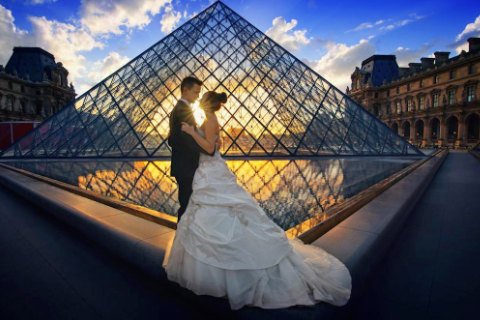 A bride and groom standing in front of the Louvre at sunset