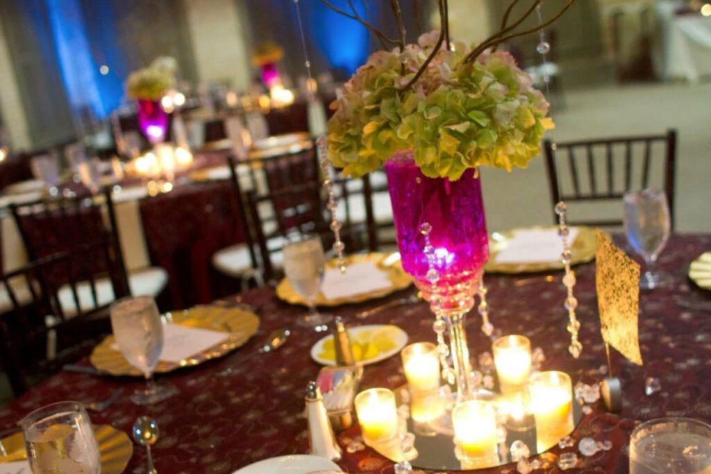 A wedding reception tablescape with a floral centerpiece in a pink vase surrounded by votive candles