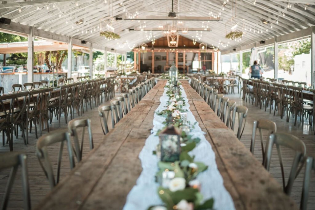 A rustic wedding reception in Fredericksburg TX with long wooden tables and open-air siding.