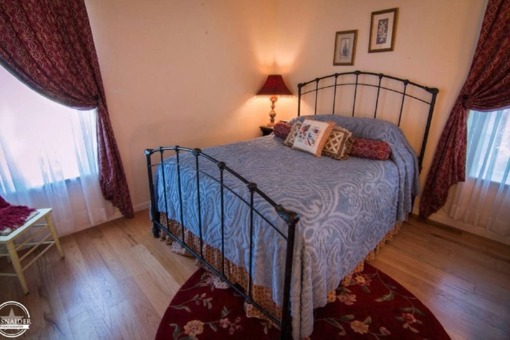 A black spindle bed with red pillows that match the red curtains and rug at The Venues and Bnbs of Monarc Ranch, a Texas hill country wedding venue in Fredericksburg TX