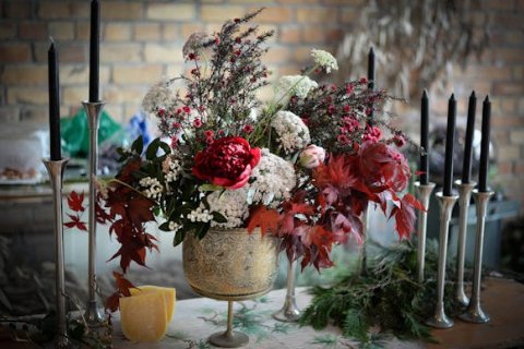 A wedding floral centerpiece with red and white fluffy blooms in an antique gold vase surrounded by black taper candles