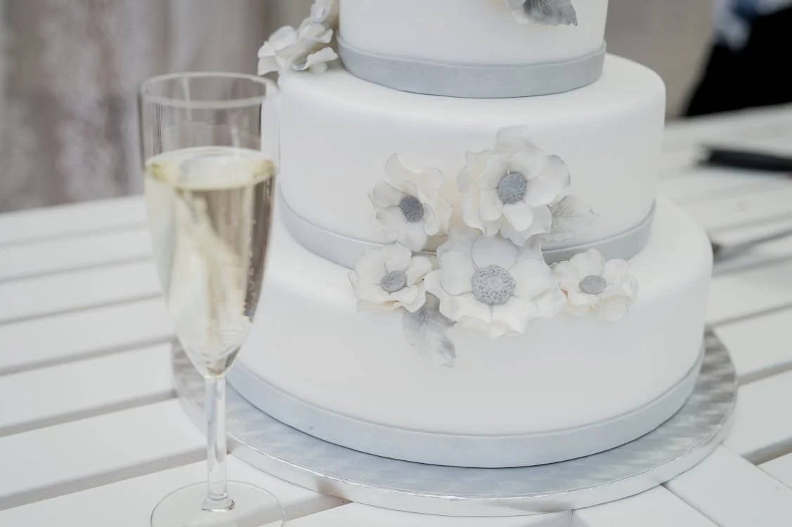 Closeup of a 3-tier white wedding cake with floral details and a glass of champagne, showing the quality of wedding cake bakers at weddings in Fredericksburg TX