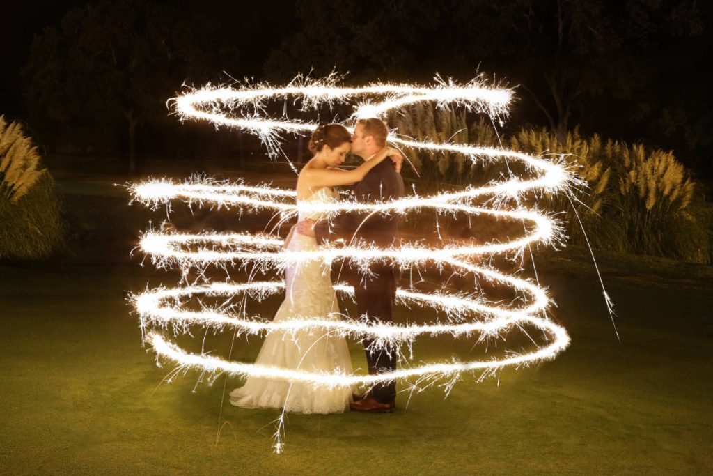 A groom kissing his bride's forehead and holding her. Sparks from wedding sparklers surround them. Image captured by Infinity Video & Photo, a wedding videographer and photographer in Fredericksburg TX