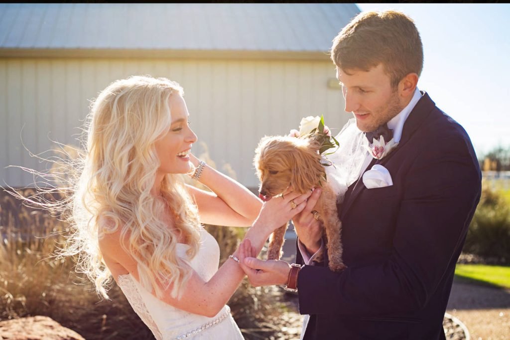 A bride and groom holding a puppy in between them. Image captured by Infinity Video & Photo, a wedding videographer and photographer in Fredericksburg TX