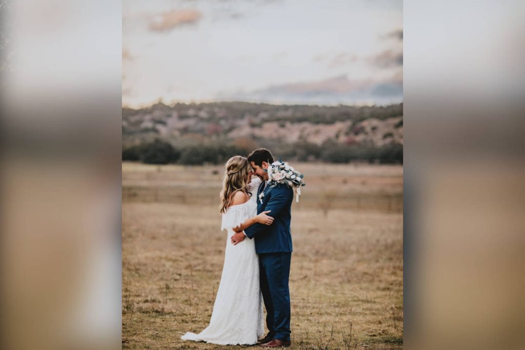 A bride and groom holding each other with their heads together in a field. Image captured by Kayla Jane Photography, a wedding photographer in Fredericksburg TX
