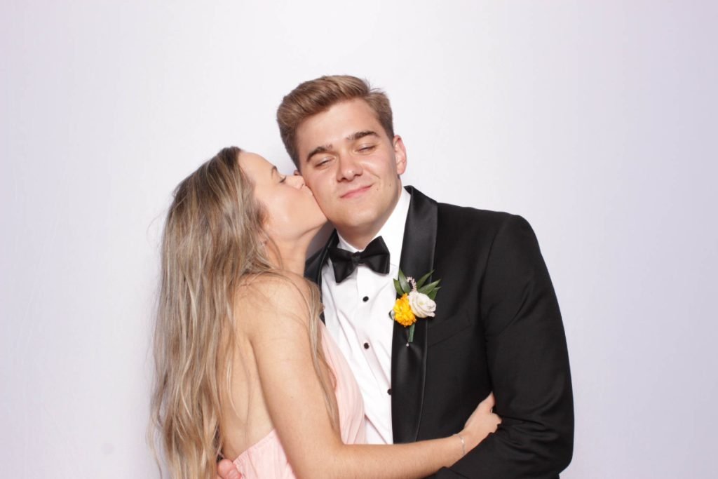 A bridesmaid in a pink dress kissing a groomsman on the cheek at a wedding photo booth in Fredericksburg TX