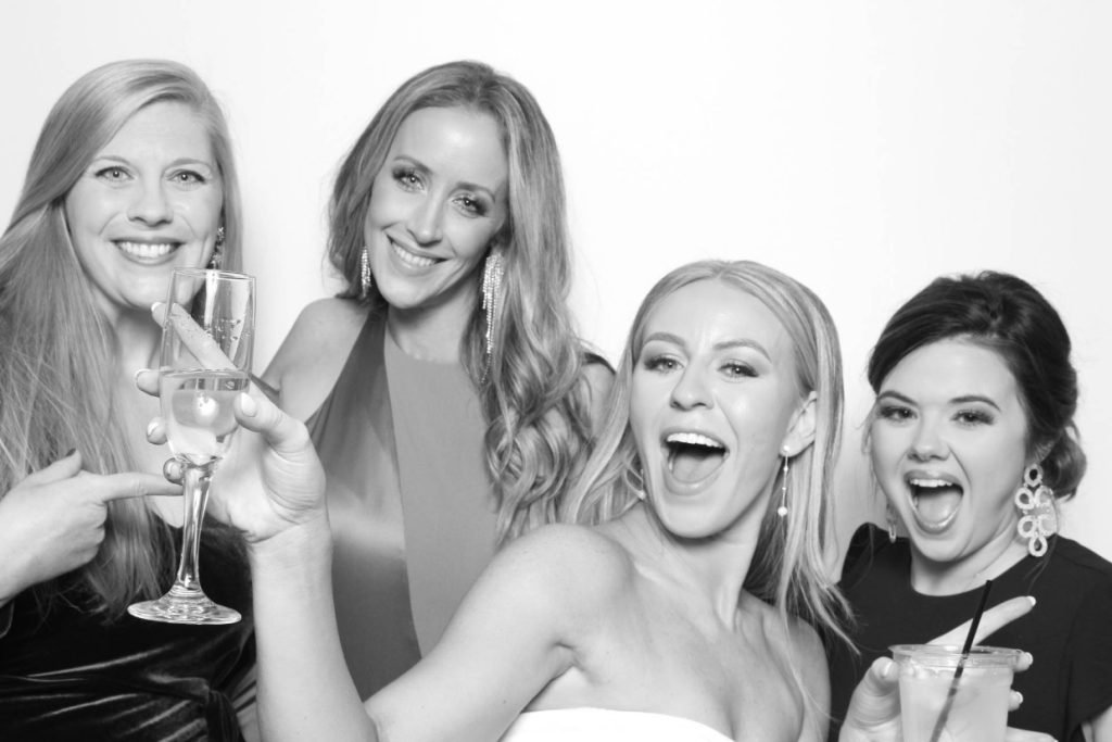 A black and white image of a bride with other ladies, taking a picture at a wedding photo booth in Fredericksburg TX