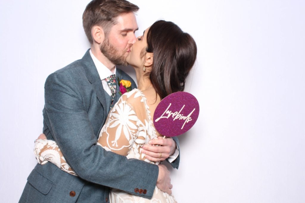 A bride and groom holding each other and kissing with a prop that says "Lovebirds"