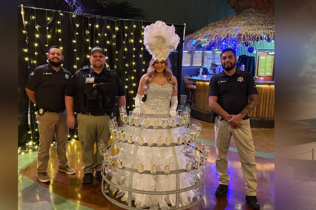 A trio of wedding security officers standing with a woman in costume serving champagne from her hoop skirt