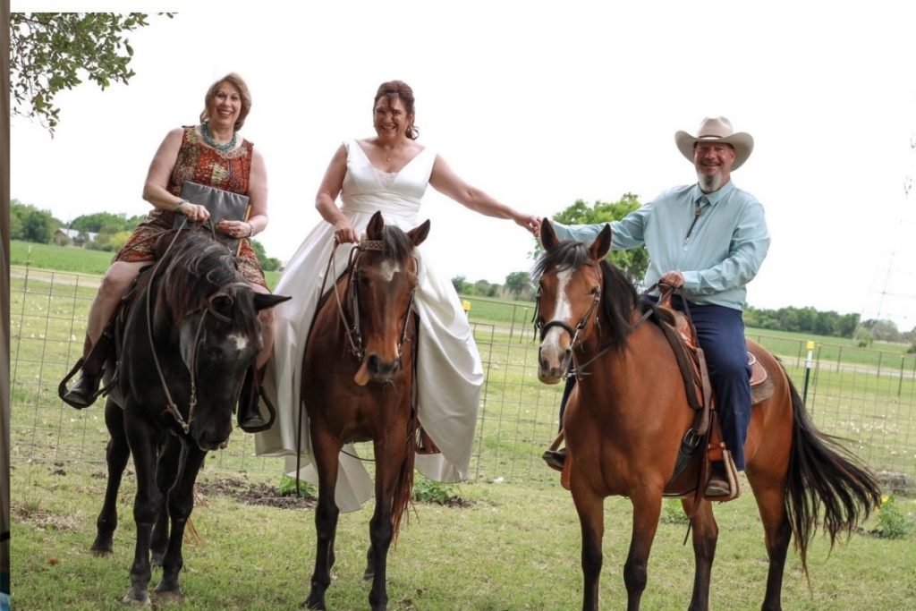 A female wedding minister on horseback riding next to a bride and groom on horseback. They represent the unique weddings in Fredericksburg TX.