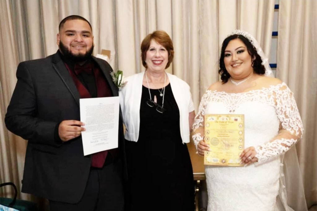 A female wedding minister standing between two newlyweds, as they hold their marriage certificate.
