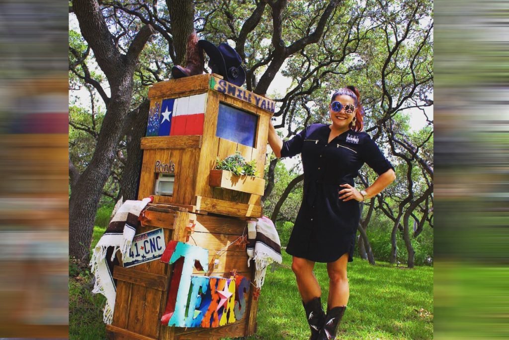 A member of the Reel Photo Booth team standing next to a rustic wedding photo booth in Fredericksburg TX